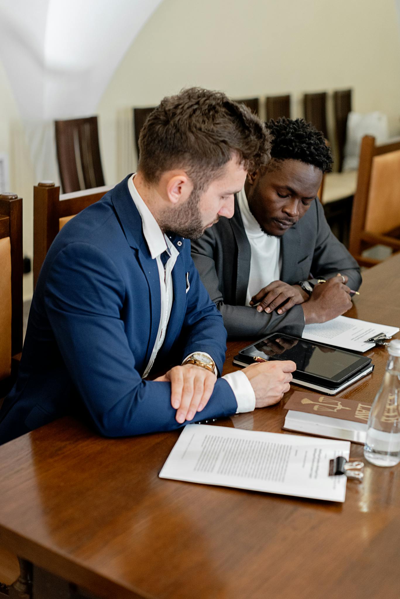 Two businessmen collaborating over documents and technology in an office setting.